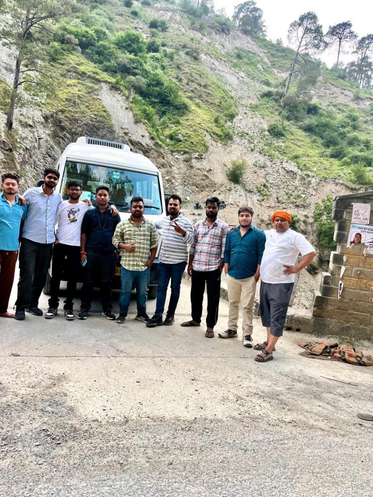 Group of travelers standing in front of a Tempo Traveller on a mountain road