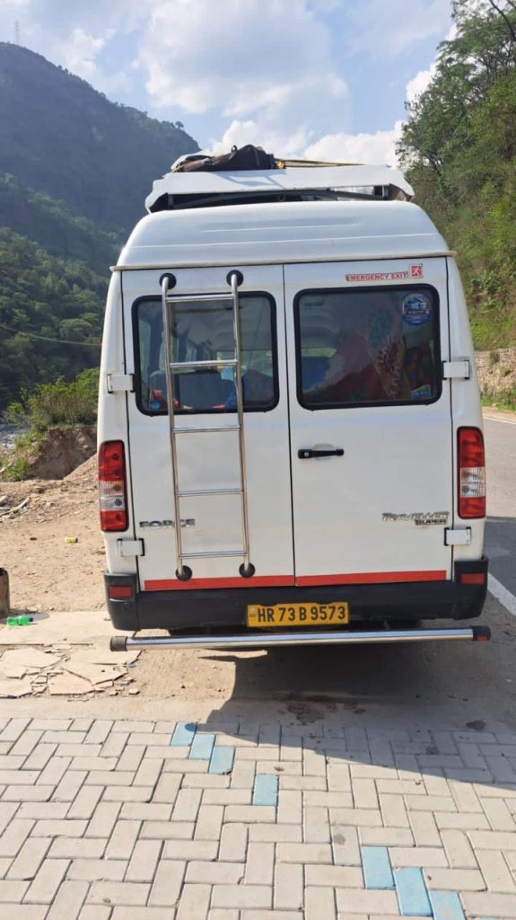 Rear view of a white Force Tempo Traveller with roof carrier and ladder